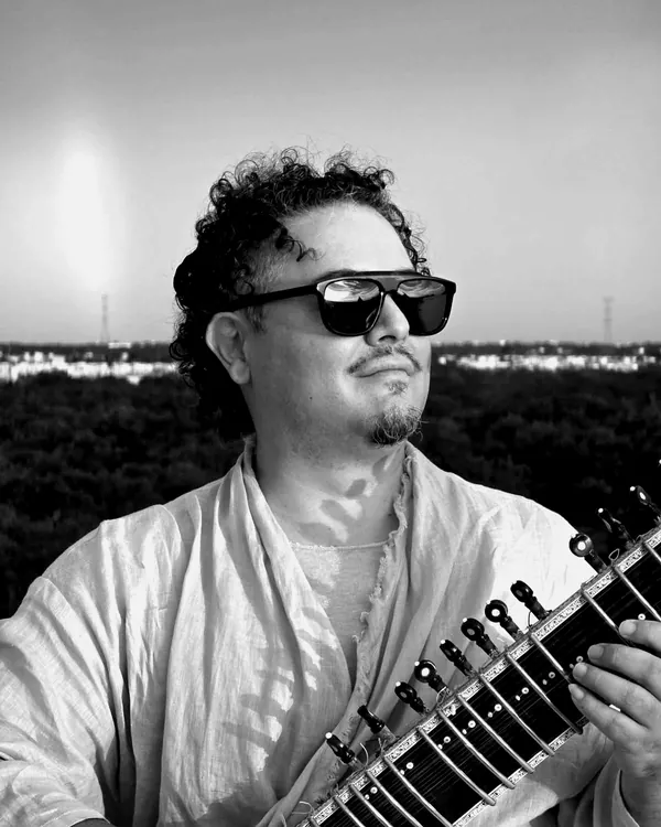 Sidartha Siliceo con lentes oscuros, tocando el sitar al atardecer